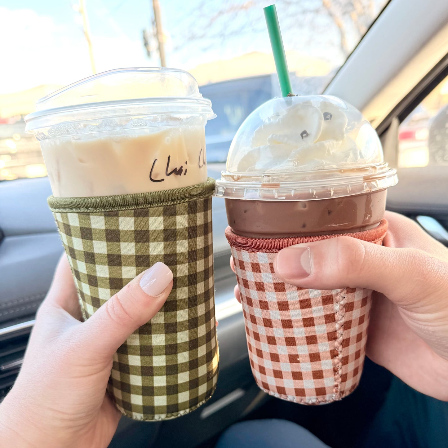 Two iced beverages in cups with lids and gingham sleeve.