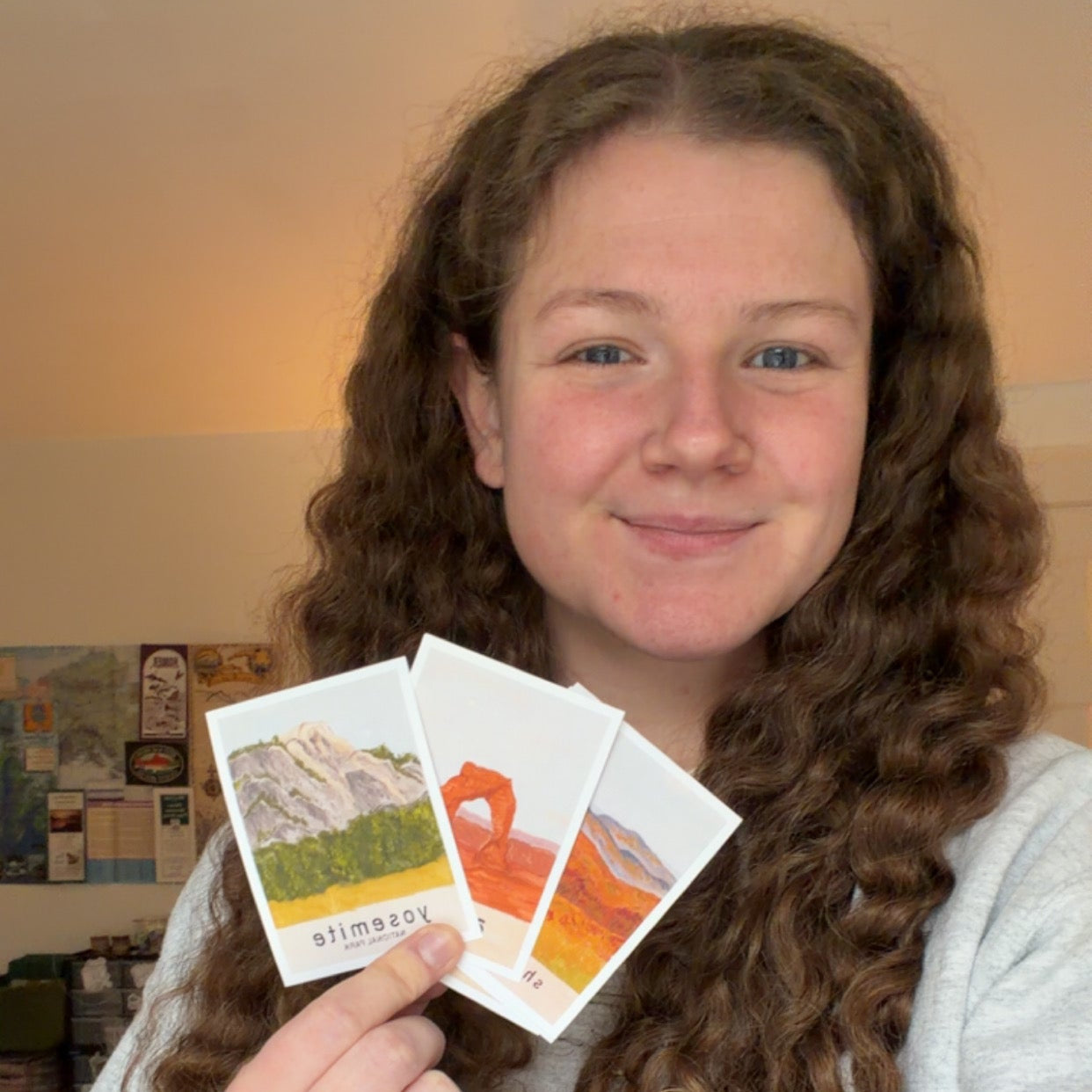 Person holding three small cards with scenic illustrations in a room setting.